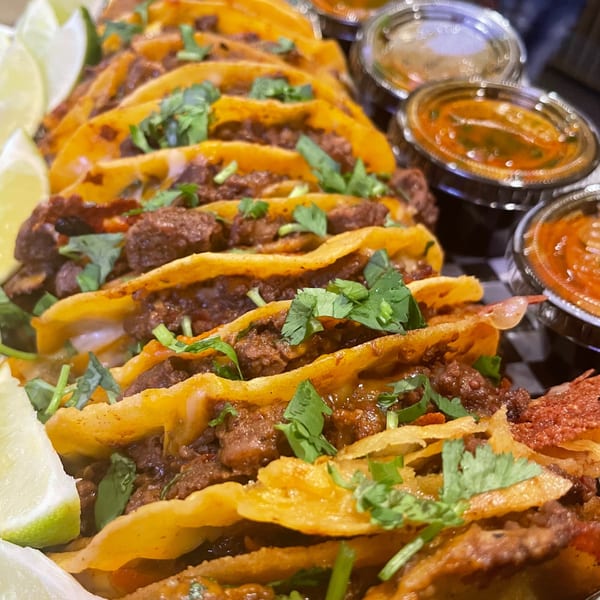 A platter of Pretty Little Tacos, garnished with cilantro and lime wedges, with dipping sauces.