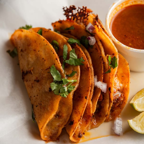 Pretty Little Tacos birria tacos with cilantro, onions, lime wedges, and a side of consommé.