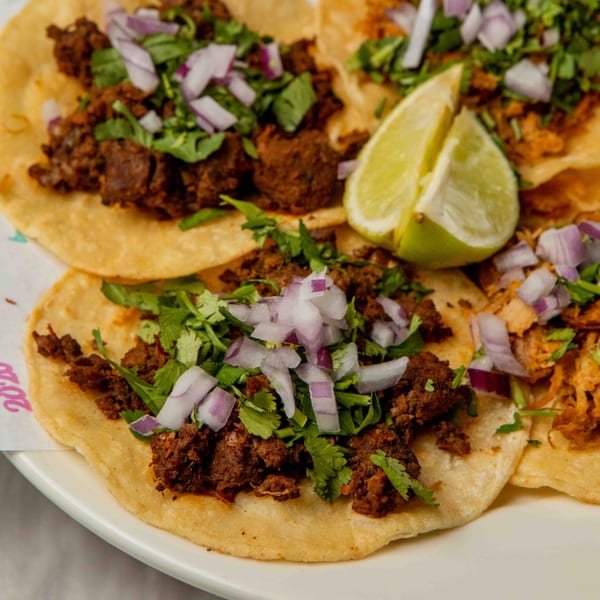 Close-up of Pretty Little Tacos' street tacos with meat, cilantro, red onions, and lime wedges.