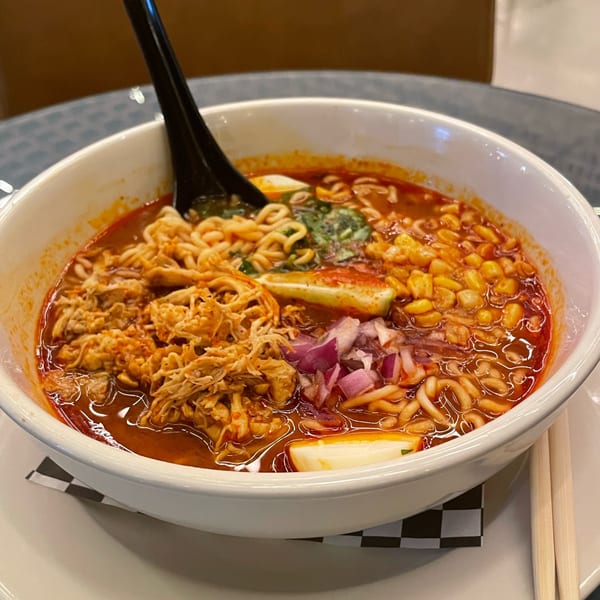 A bowl of ramen with shredded chicken, corn, red onions, and a hard-boiled egg.