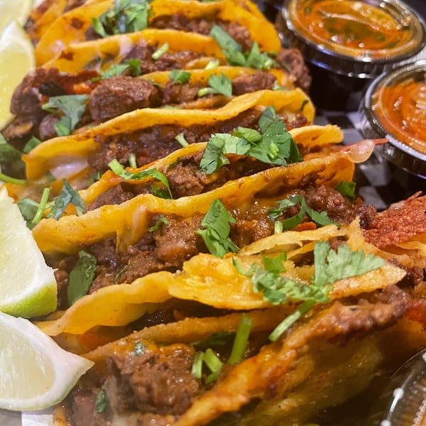 Close-up of several Pretty Little Tacos with meat, cilantro, and lime wedges, with dipping sauces.