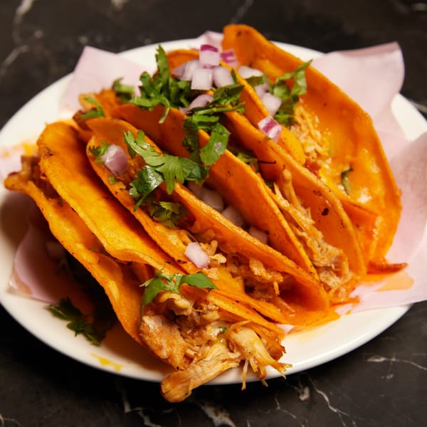 A plate of Pretty Little Tacos, with orange tortillas, shredded meat, cilantro, and diced red onions.