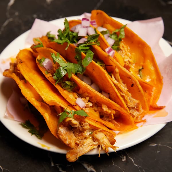 A plate of Pretty Little Tacos, featuring several birria tacos with cilantro and diced red onions.