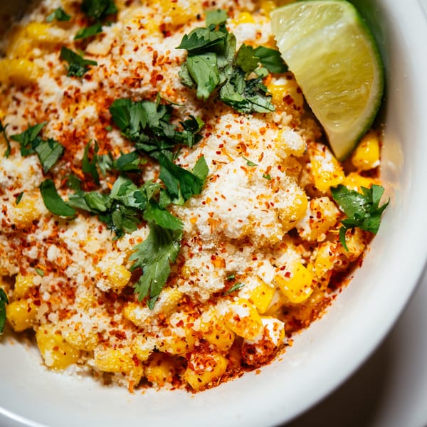 Close-up of Mexican street corn with cheese, chili powder, cilantro, and a lime wedge.